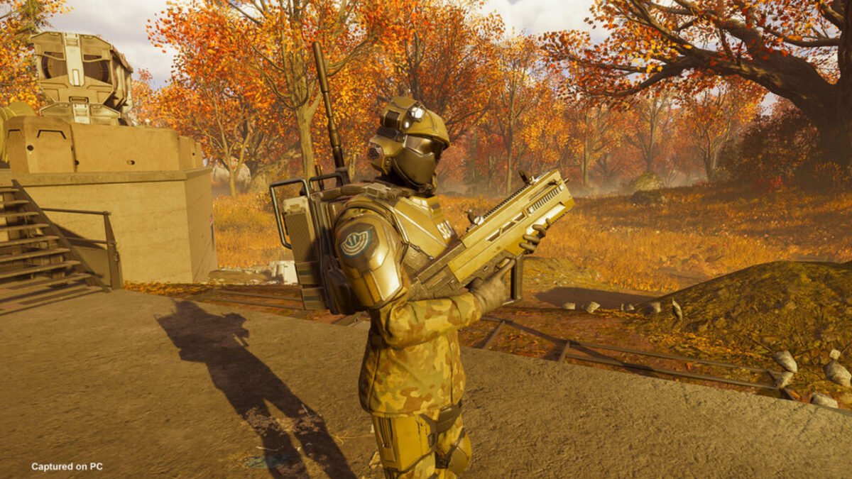 Official Xbox Wire Helldivers 2 screenshot showing a yellow-armored SEAF squad member holding a radio in an autumn battlefield.